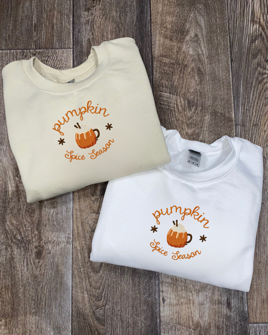 Two folded sweatshirts with 'Pumpkin Spice Season' embroidered text on a wooden surface