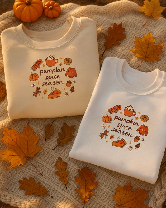 Two folded sweatshirts with embroidered 'pumpkin spice season' design on a textured surface with autumn leaves.