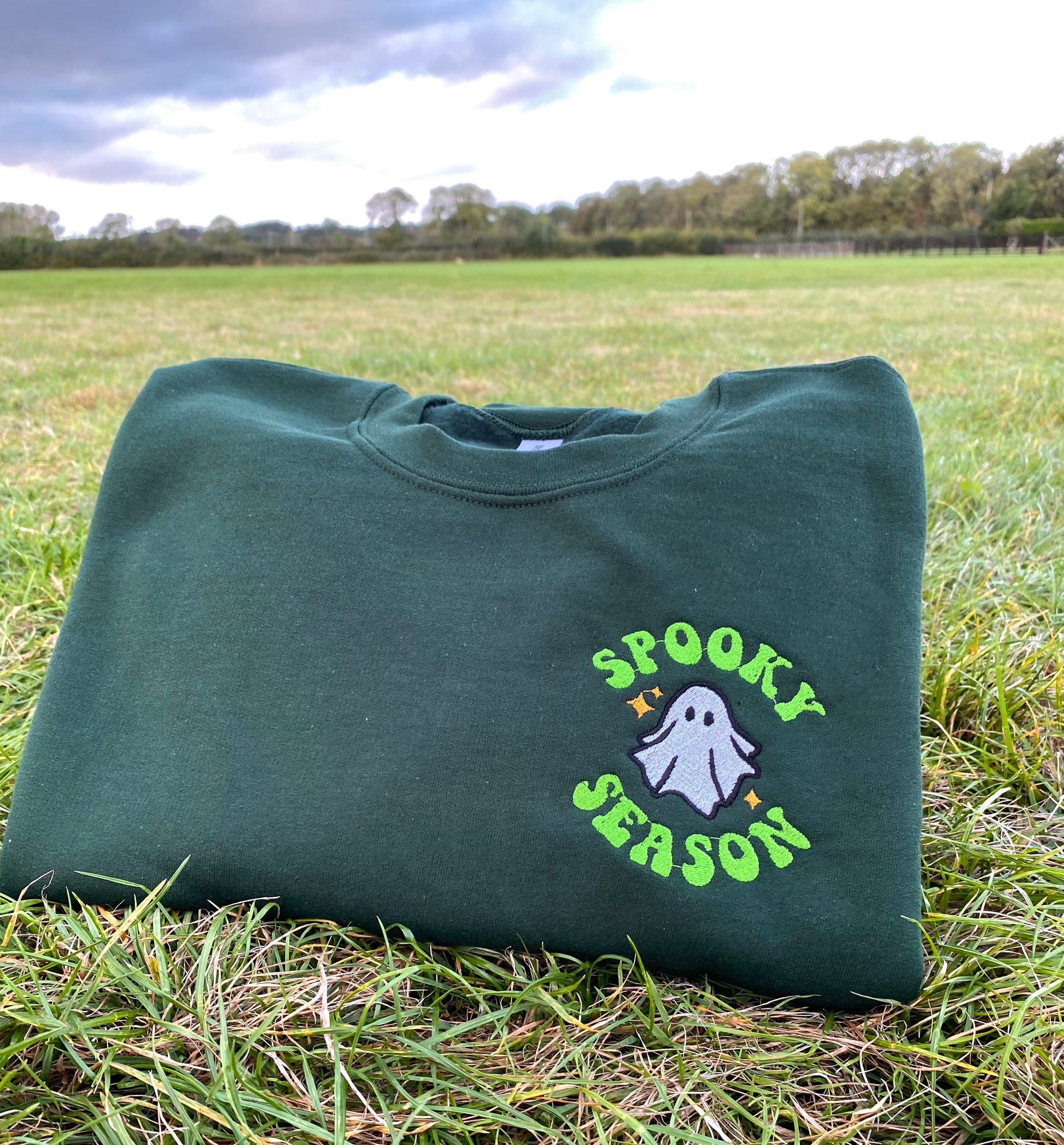 Green sweatshirt with 'Spooky Season' embroidered design on grass