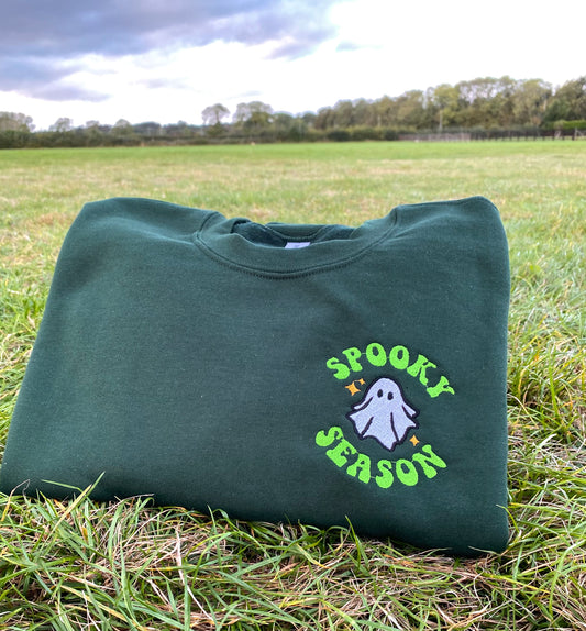 Green sweatshirt with 'Spooky Season' embroidered design on grass