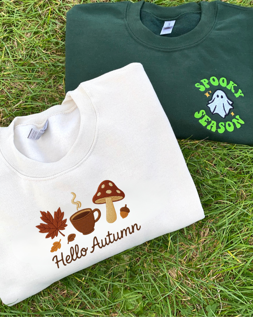 Two sweatshirts, one with 'Hello Autumn' design and the other with 'Spooky Season' design, on grass.