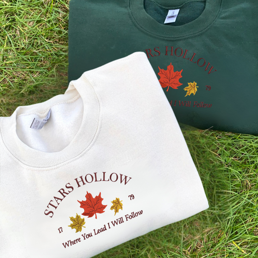 Two sweatshirts with 'Stars Hollow' text and leaf designs on grass.