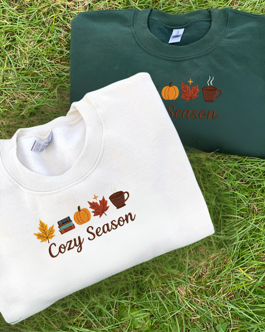 Two sweatshirts with embroidered  'Cozy Season' design on grass