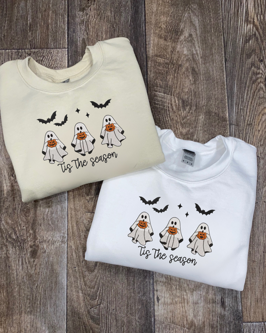 Two Halloween-themed sweatshirts with ghost and pumpkin embroidered designs on a wooden surface.