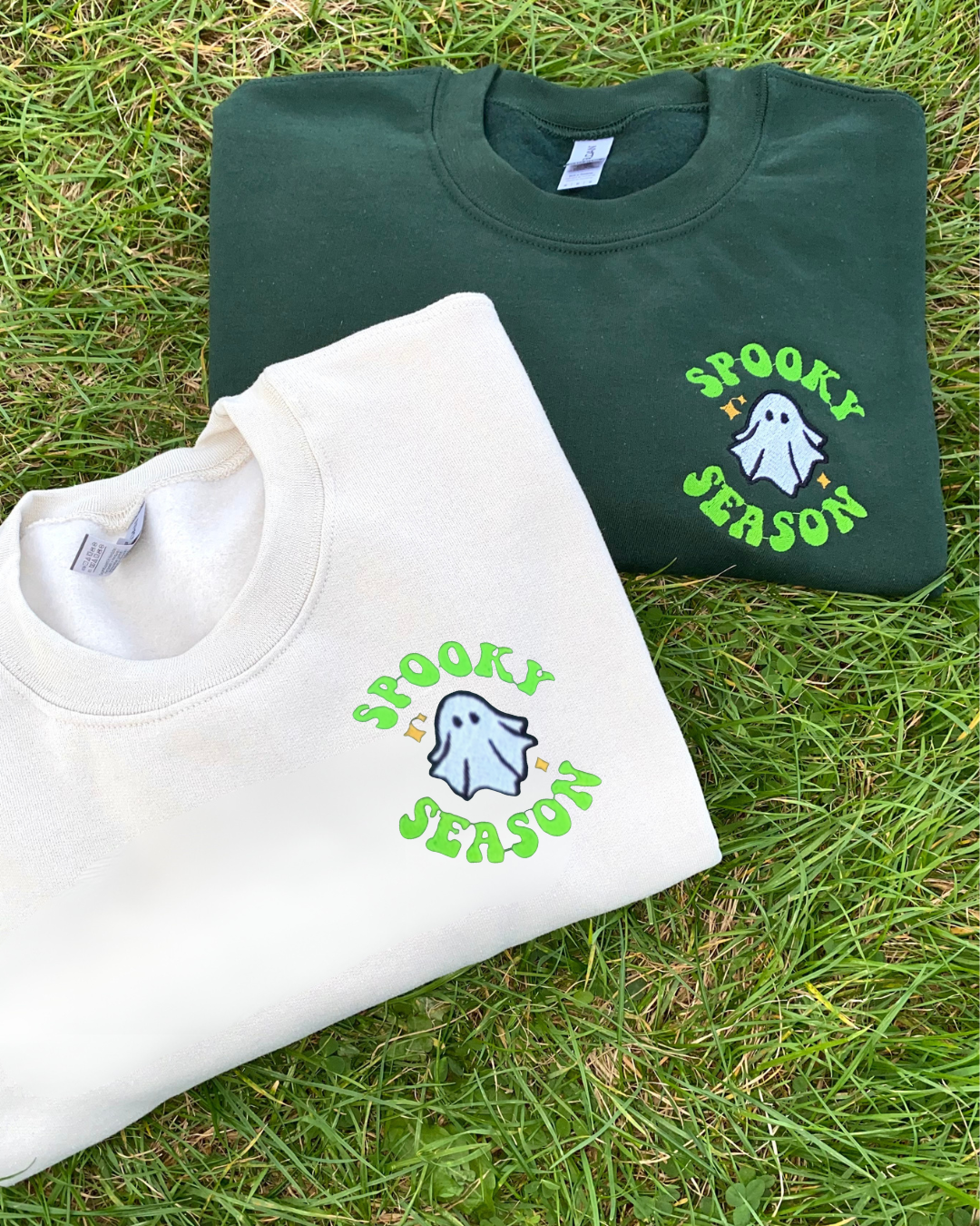 Two folded sweatshirts with 'Spooky Season' embroidery design on grass